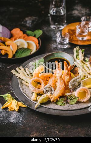 Battered fried shrimp and vegetables on platter with dark sauce and raw ingredients in background Stock Photo