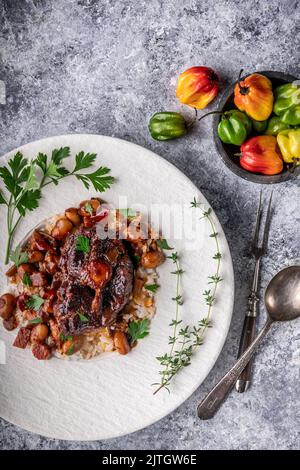 Oxtail with bone, sauce and rice on white plate with herb garnish and peppers in bowl Stock Photo