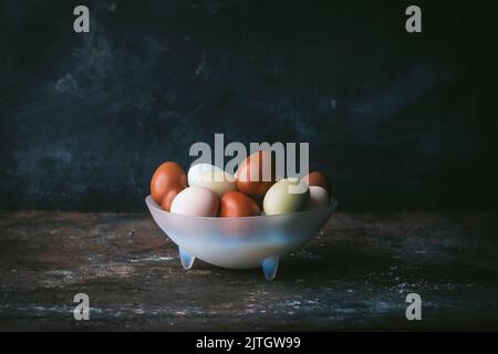 Naturally colored eggs in a pale blue transluscent glass bowl on dark background Stock Photo