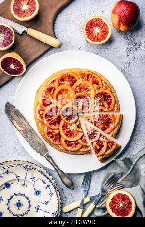 Sliced Blood Orange Cake, with layered citrus, on white platter, with cutting board and cut blood oranges Stock Photo