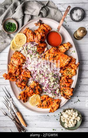 Grilled chicken with spicy sauce and cabbage slaw on large platter on white wood backgroun Stock Photo