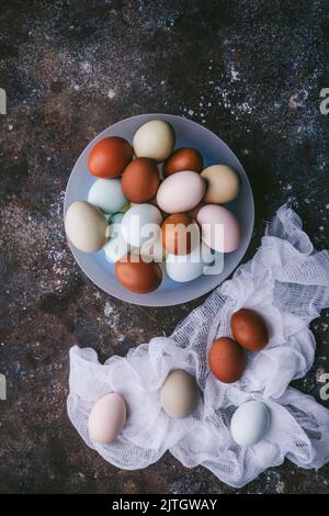Flat lay of naturally colored eggs in a bowl and on cheesecloth on dark background Stock Photo