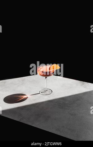 An orange cocktail in a cocktail glass, with a slice of ornage garnish. Against a marble and black background. Stock Photo