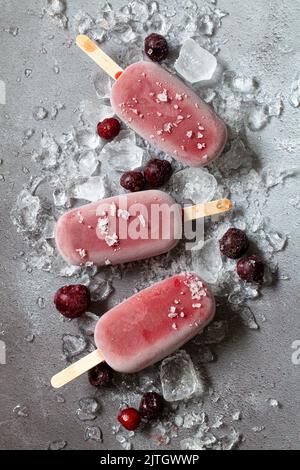 Three cherry flavoured popsicles (ice lollies) on crushed ice with frozen cherriese. Stock Photo