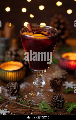 Mulled wine in a stemmed glass with orange and spice garnish. In a festive setting with candles and fairy lights. Stock Photo