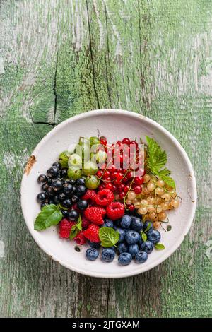 Mix of fresh berries with leaves in vintage ceramic colander on green rustic wooden background Stock Photo