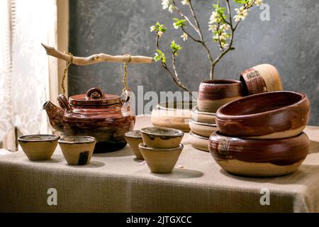 Japanese Asian style table setting with empty craft ceramic tableware, brown rough bowls and cups on linen tablecloth, decorated by ikebana spring flo Stock Photo
