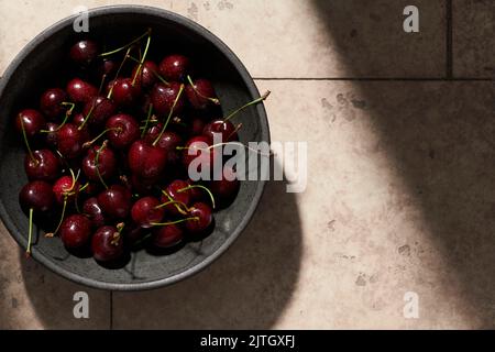 Dark red cherries spritzed with water in a dark bowl on a tile surface. Stock Photo