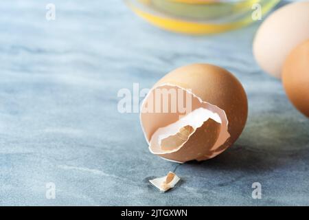 A cracked eggshell with two whole eggs and an egg yolk in a glass bowl. Stock Photo
