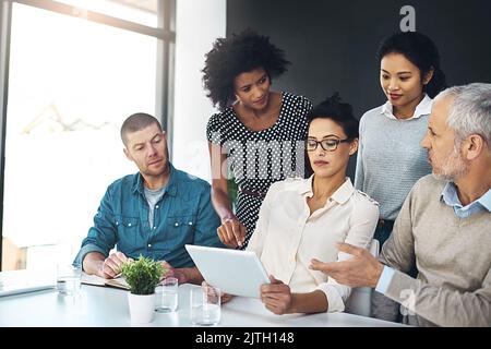 Working through the details. a group of colleagues discussing something on a digital tablet together. Stock Photo