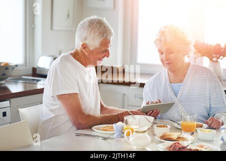 Theyre becoming tech savvy seniors. a senior couple using a digital tablet while having breakfast at home. Stock Photo