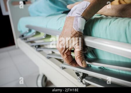Wrinkled hand of a female elderly patient on the handrail of a hospital bed Stock Photo
