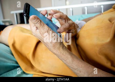 Asian female senior patient in hospital using smartphone for entertainment Stock Photo