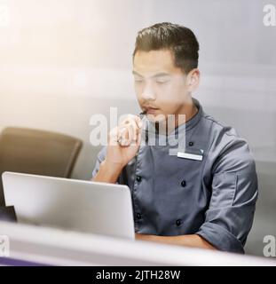 What to put on the menu. a thoughtful young man working on his laptop. Stock Photo