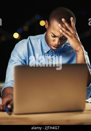 Running out of time. a young man looking stressed while working late night on his laptop. Stock Photo