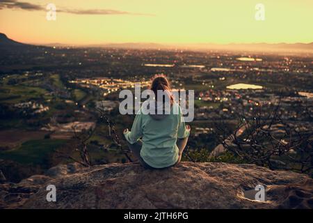 Meditating at the top. Rearview shot of a sporty young woman meditating outdoors. Stock Photo