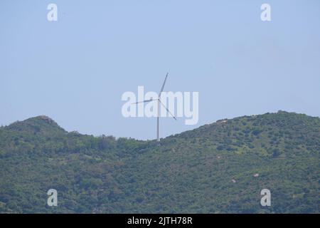 A wind turbine on an evergreen hill against a blue sky in Lamma Island, Hong Kong Stock Photo