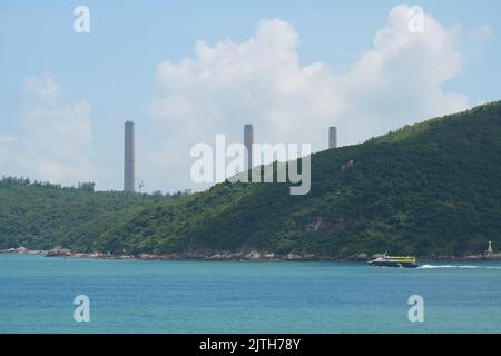 A power plant on an evergreen hill against a blue sky with a lake in the foreground in Lamma Island Stock Photo