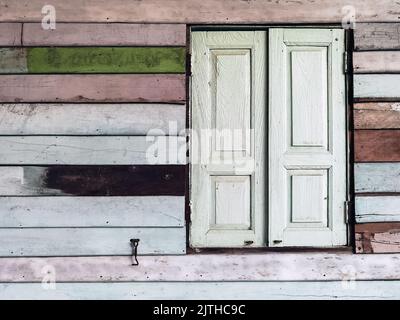 Old grunged wooden window frame painted white vintage with old colourful plywood wall. Antique window frame and old panes. Old closed window and plank Stock Photo