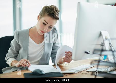 Fact-checking all the details. a young businesswoman reading some paperwork in an office. Stock Photo