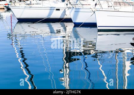 Sailing yachts moored in marina on a sunny day reflect in rippled sea water. Abstract background photo Stock Photo