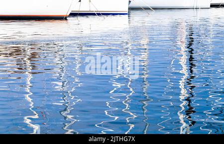 Rippled sea water with reflections of yachts moored in marina on a sunny day. Abstract background photo Stock Photo
