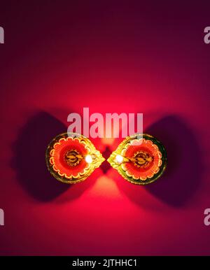 Happy Diwali, Deepavali Hindu Festival of lights celebration. Diya oil lamp lit on red background, top view. Stock Photo
