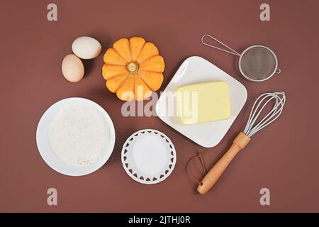 Pumpkin pie ingredients and baking tools on brown background Stock Photo