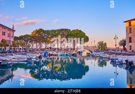 The bright sky over the Porto Vecchio port and small boats and outdoor restaurants around the port, Desenzano del Garda, Italy Stock Photo