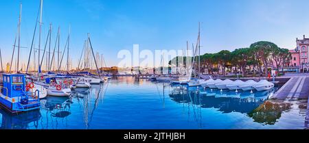 The joyful evening walk with a view on Lake Garda Port, sail yachts and alley with pines in background, Desenzano del Garda, Italy Stock Photo