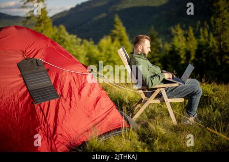 Man works on laptop at campsite in the mountains Stock Photo