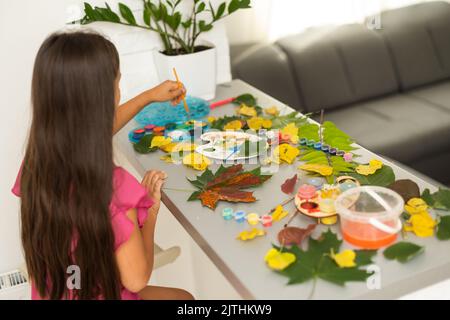 child paints leaves with paints, draws a picture, making prints of leaves. Childrens creativity in nature. Outdoor. Summer. Stock Photo