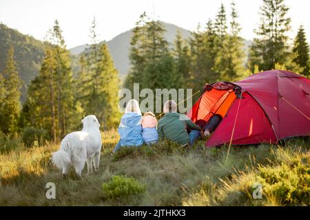 Family with a kid sit together at campsite near the tent in the mountains Stock Photo