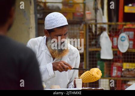 A muslim man peeling off the skin of pineapple to sell in street Stock Photo