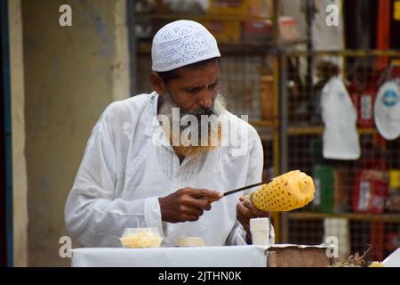 A muslim man peeling off the skin of pineapple to sell in street Stock Photo