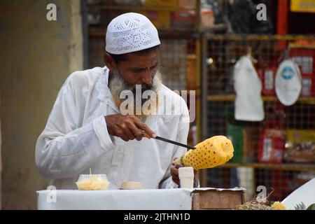 A muslim man peeling off the skin of pineapple to sell in street Stock Photo