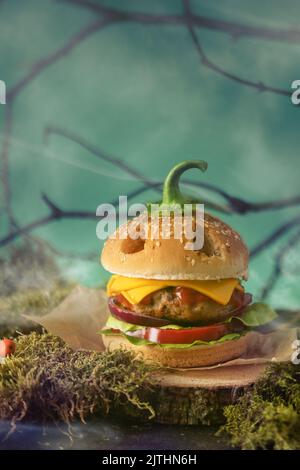 Halloween burger in a shape of pumpkin head jack lantern in a mystery forest. Scary cheeseburger on halloween party. Stock Photo