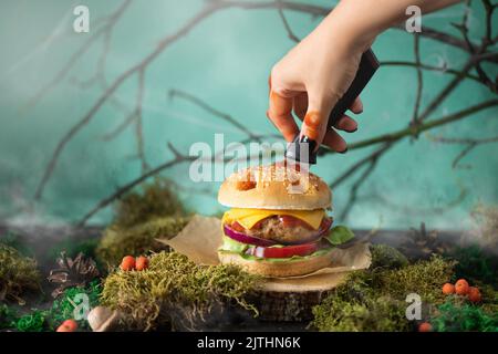 Halloween burger in a shape of pumpkin head jack lantern in a mystery forest. Scary cheeseburger on halloween party. Stock Photo