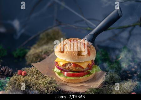 Halloween burger in a shape of pumpkin head jack lantern in a mystery forest. Scary cheeseburger on halloween party. Stock Photo