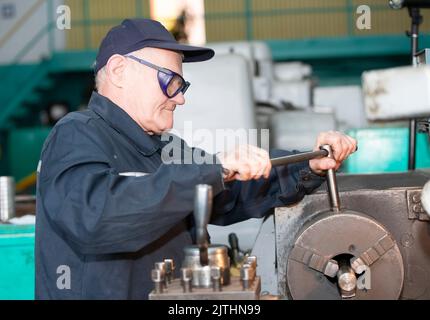 Turning production An elderly man works at a lathe. Turning works. Stock Photo