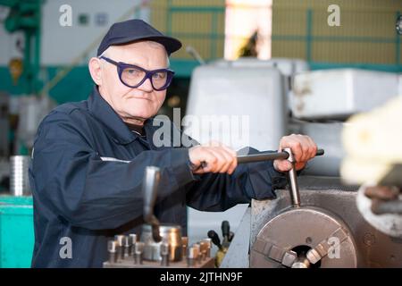 Turning production An elderly man works at a lathe. Turning works. Stock Photo