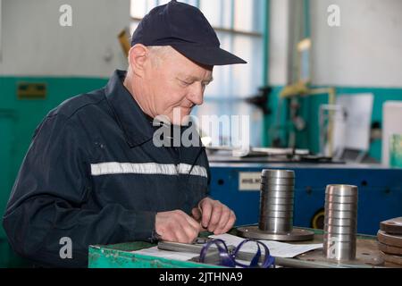 Turning production An elderly man works at a lathe. Turning works. Stock Photo