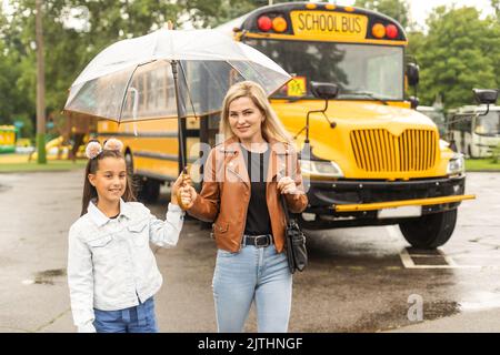 Back to school. Pupils of primary school near school bus. Happy children ready to study. little girl with mom going to bus Stock Photo