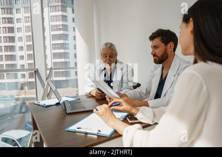 Two doctors in white uniform consult female patient at meeting in private clinic Stock Photo
