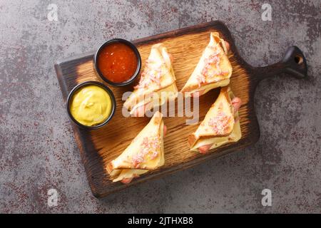 Homemade toasted sandwich with Vienna sausages and melted cheese served with ketchup and mustard close-up on a wooden board on the table. horizontal t Stock Photo