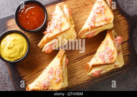 Hot sandwich with Vienna sausages and melted cheese served with ketchup and mustard close-up on a wooden board on the table. horizontal top view from Stock Photo
