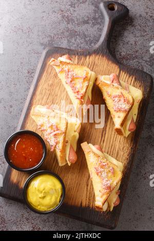 Hot toast with sausages and cheese served with ketchup and mustard close-up on a wooden board on the table. vertical top view from above Stock Photo