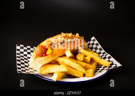 Frankfurt sausage with fried onion accompanied with french fries on a white plate over a black background Stock Photo