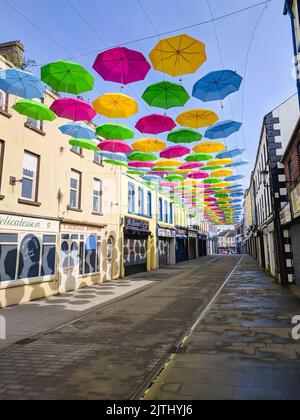 Multicoloured umbrellas suspended above an empty shopping street in a small town. Stock Photo