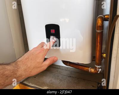 Man setting electric boiler for home underfloor heating system, selective focus Stock Photo